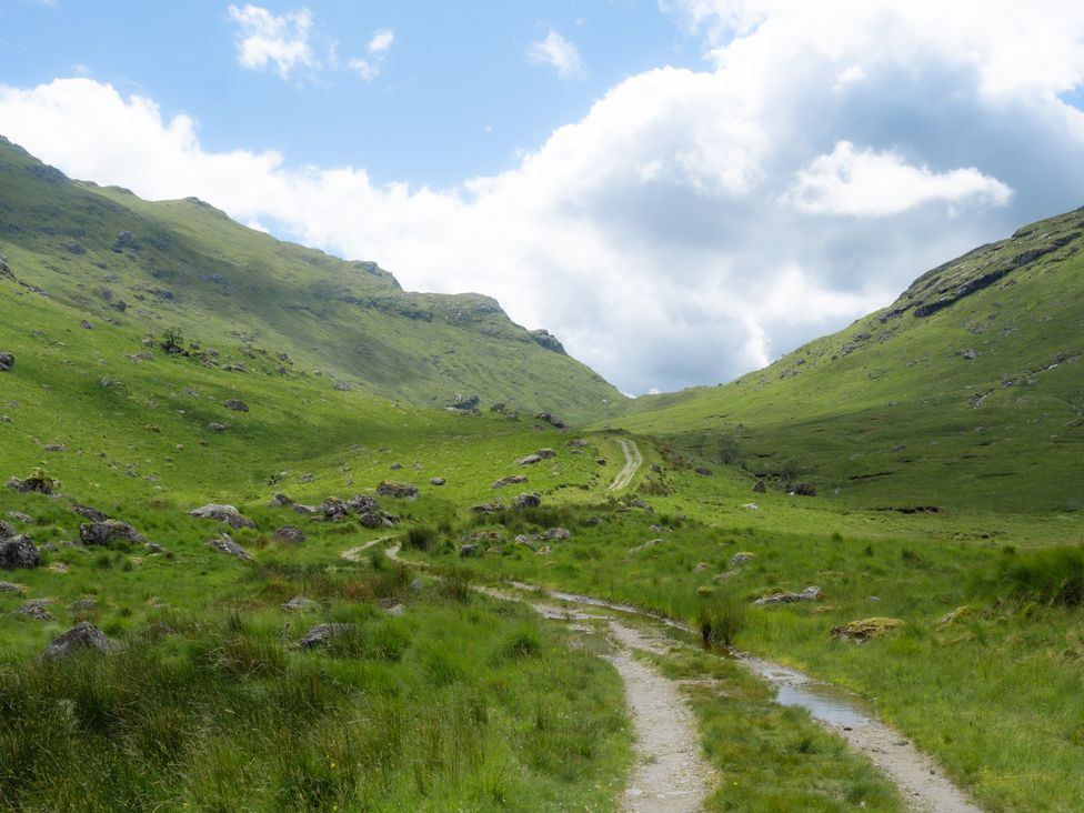 A trail between mountains and grass at Curlew Cottage in Crianlarich
