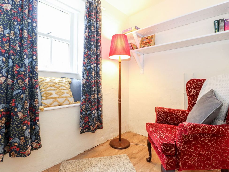 A snug with a red armchair and decorative curtains at Irt Cottage Seascale