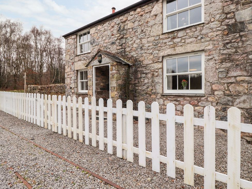 A stone building with a white fence and gravel path at Irt Cottage in Seascale