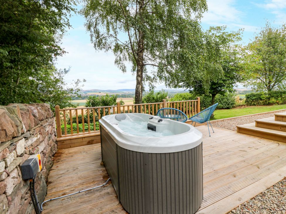 An outdoor space with a hot tub and chair at Doocot Wood Cottage Forfar