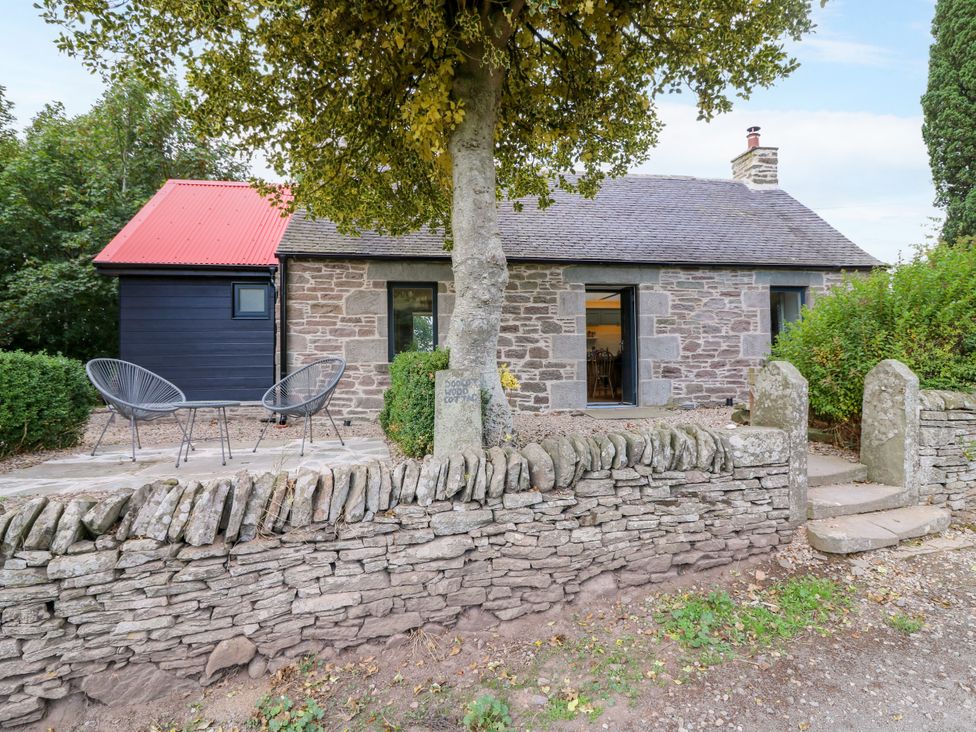 A cottage with a stone wall and chairs outside at Doocot Wood Cottage in Forfar
