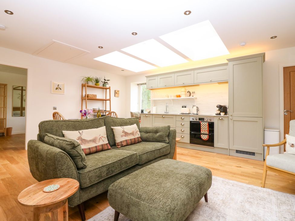 A living room with a sofa and kitchen area at Doo'cot Wood Cottage in Forfar