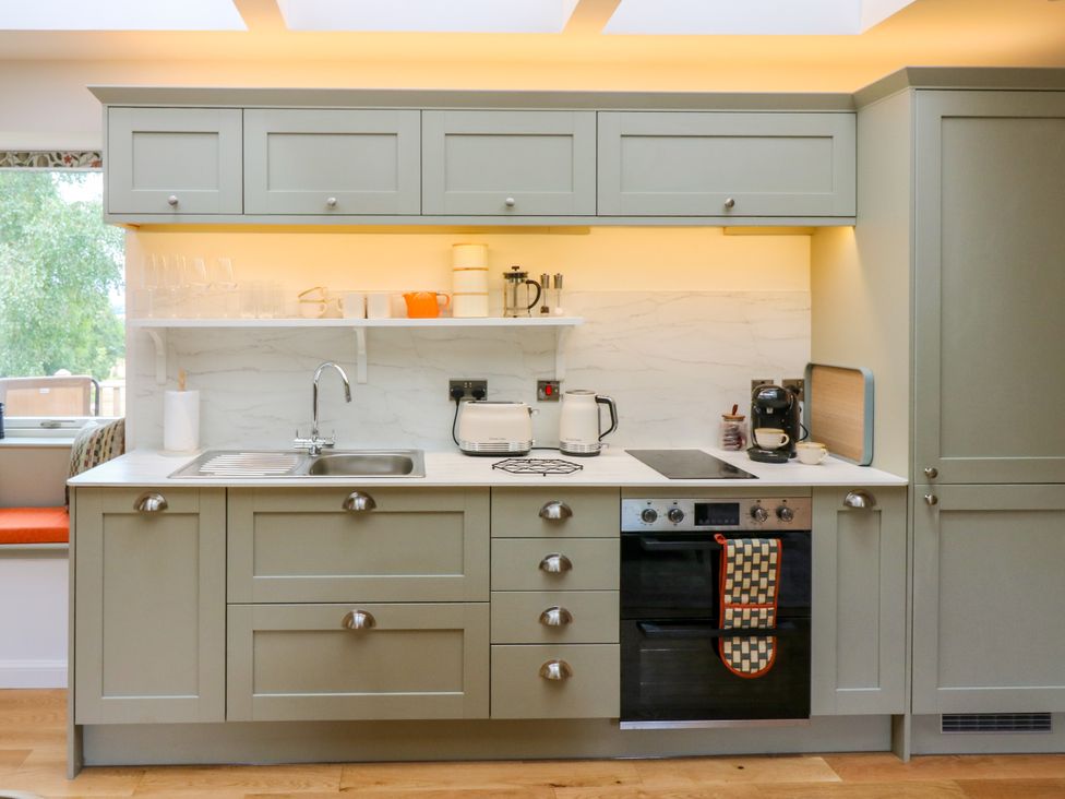 A kitchen with cabinetry, sink, and kitchen appliances at Doo'cot Wood Cottage in Forfar