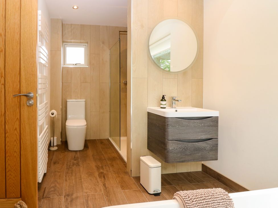 A bathroom with a sink, toilet, shower, and mirror at Doo'cot Wood Cottage in Forfar