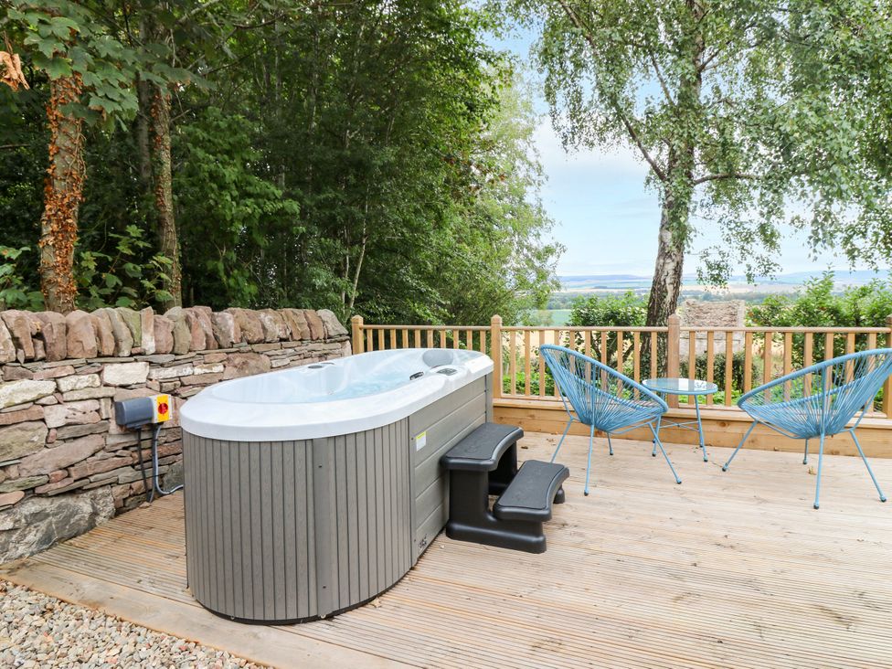 An outdoor area with a hot tub and seating at Doocot Wood Cottage in Forfar