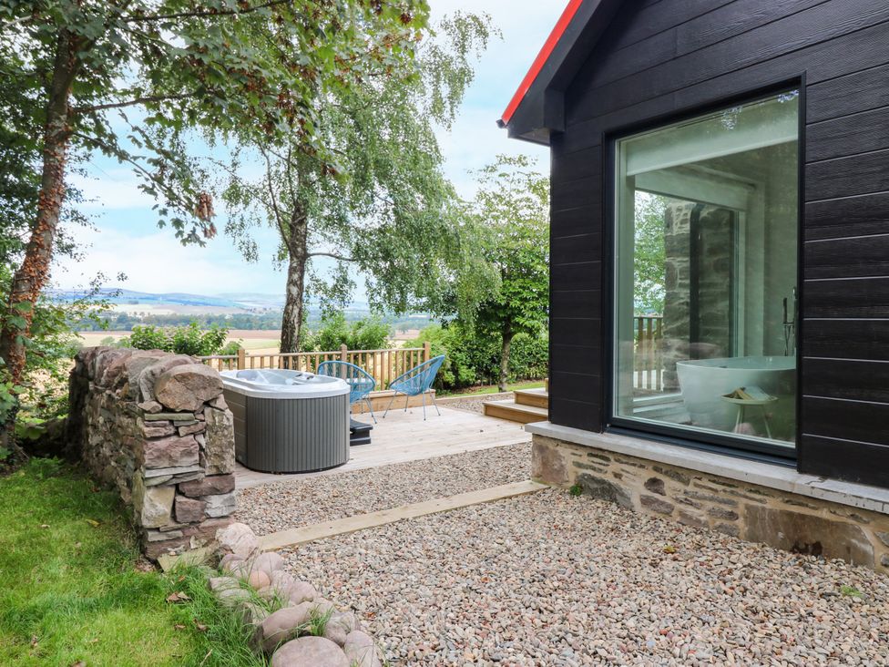 A deck with a hot tub and chairs at Doocot Wood Cottage in Forfar