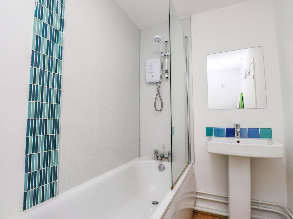A bathroom with a bathtub, shower, sink, and mirror at Flat 16 Criccieth