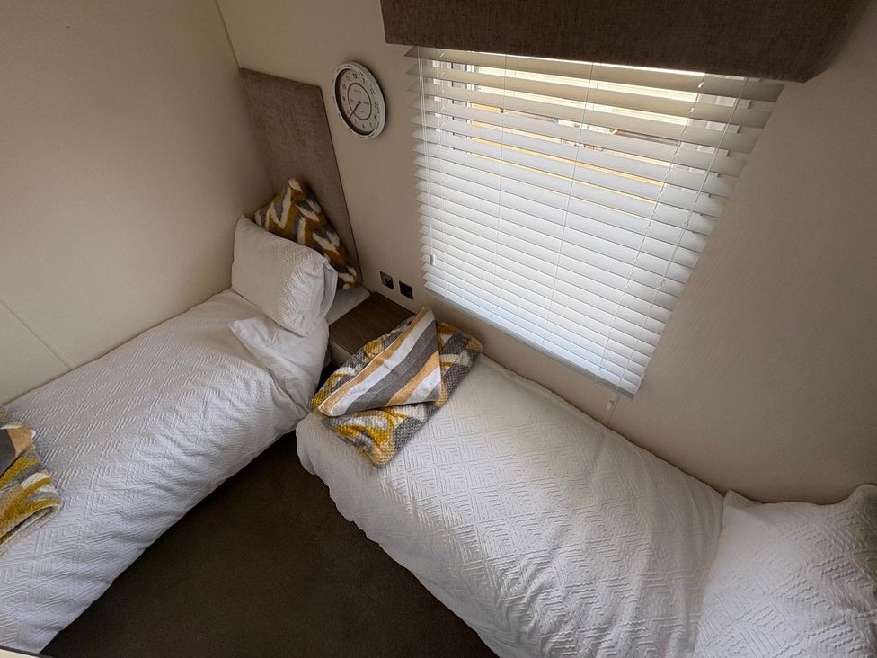 A bedroom with two single beds and a wall clock at Lyons Robin Hood Rhyl