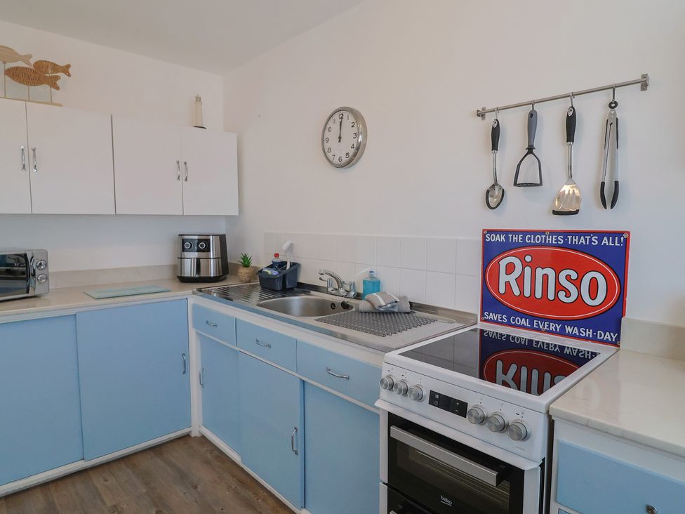 A kitchen with cabinets, sink, clock, and stove at 16 Old Shipyard Centre, West Bay