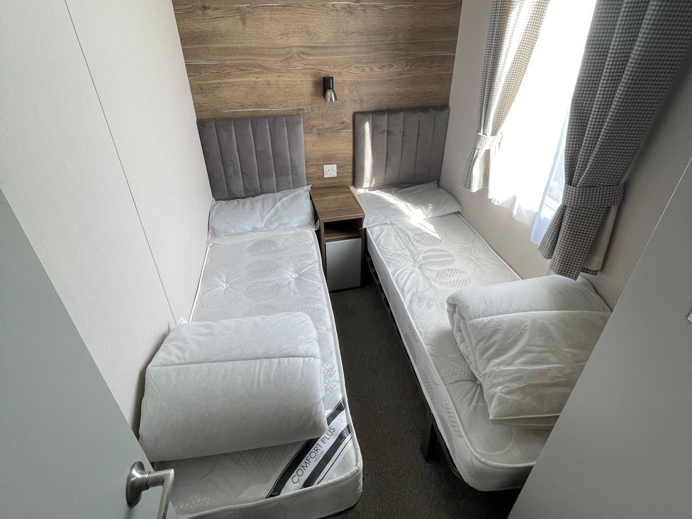 A bedroom with two single beds and a nightstand with wall lamp at Unity Beach in Burnham-on-Sea