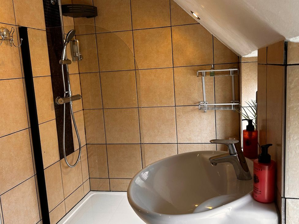 A bath with a shower and soap dispensers at Old Cottages: 3 Bed in Ripon