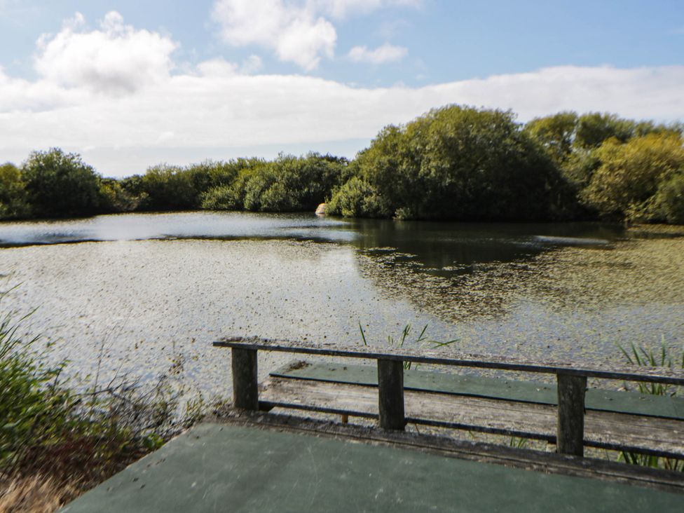 A scenic view of a pond with a bench in the foreground at May Cottage St Davids