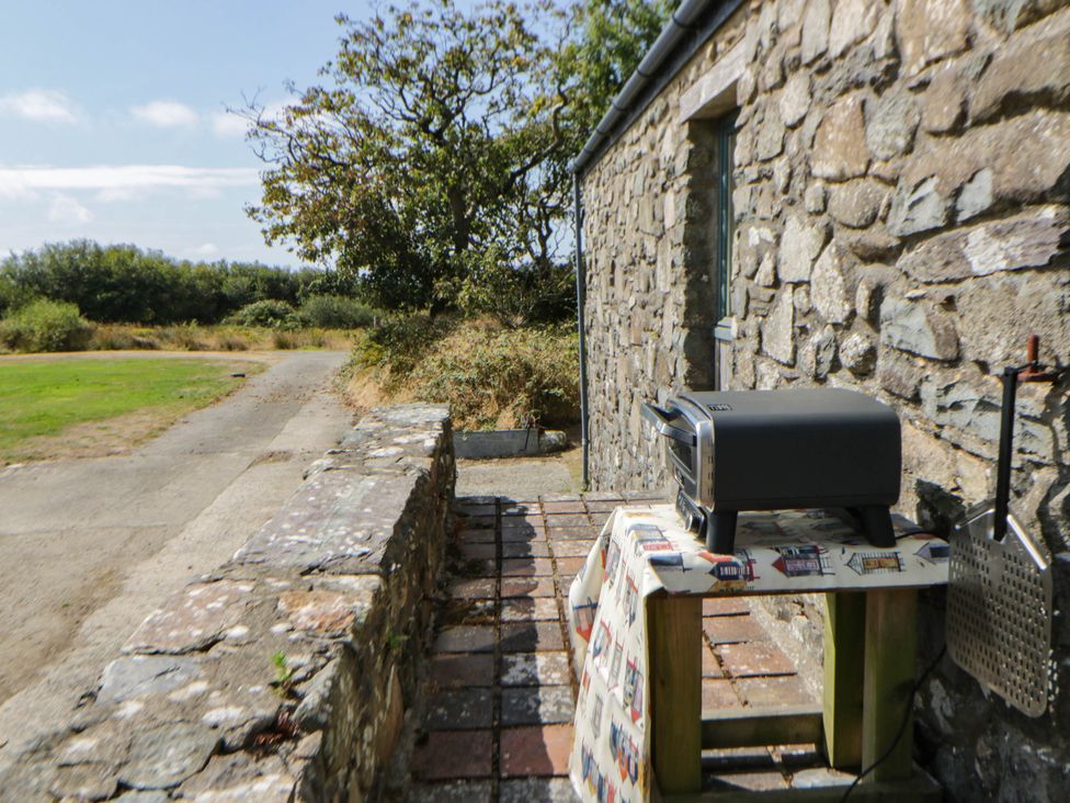 An outdoor area with a grill on a table beside a stone wall at May Cottage St Davids