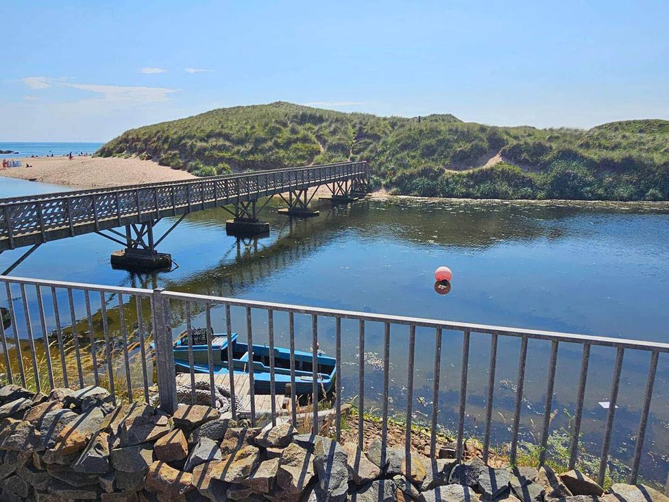 A wooden bridge over a river with a boat and a beach at 2 Bed Cottage Sleeps 4 Harbour Sea View Cruden Bay
