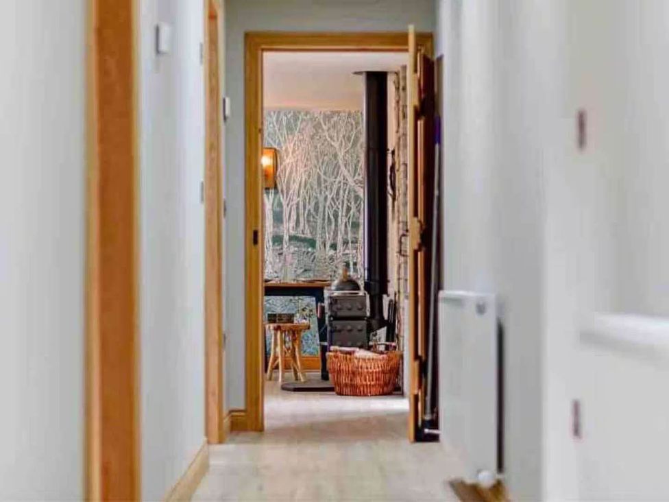 A hallway leading to a room with a wood stove and furniture at The Old Barn in Forth