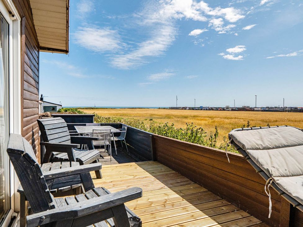 An outdoor terrace with wooden chairs and a table overlooking grass and the sea at 