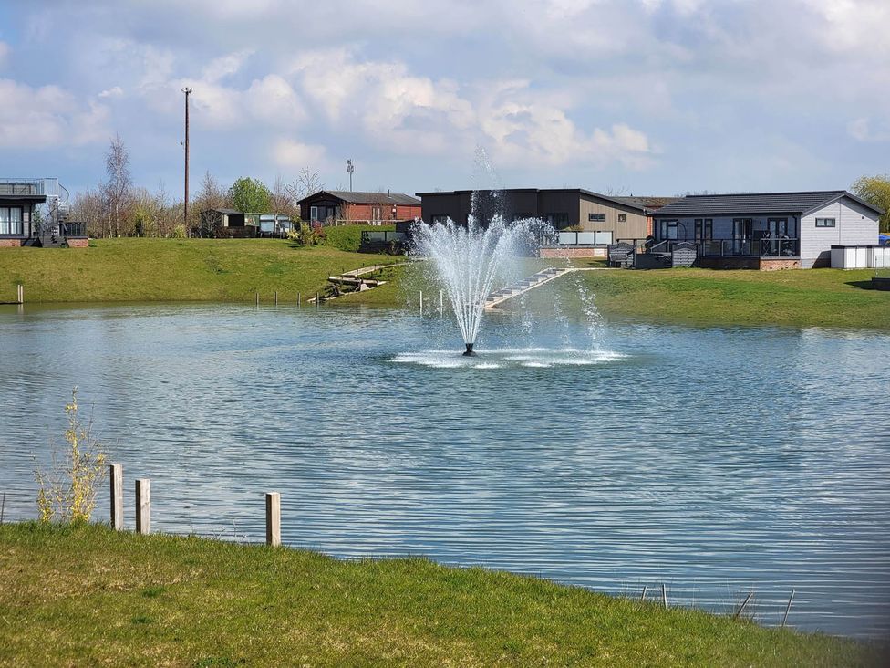 A fountain in a lake with houses behind at Pet Friendly 2Bed Luxury Lodge in Routh HotTub Heron Lakes Luxury Lodge Park near Beverley