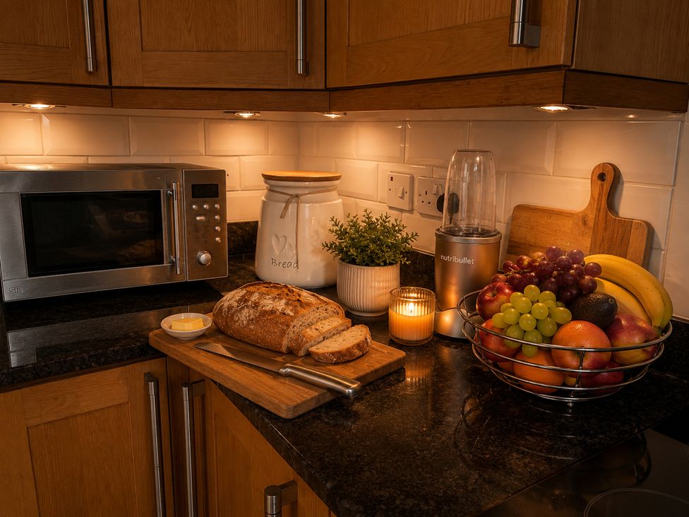 A kitchen with bread, microwave, fruits in a bowl, and a nutribullet at 3Bed House Sleeps 7 Parking Garden Pets Ok in Lytham St. Annes