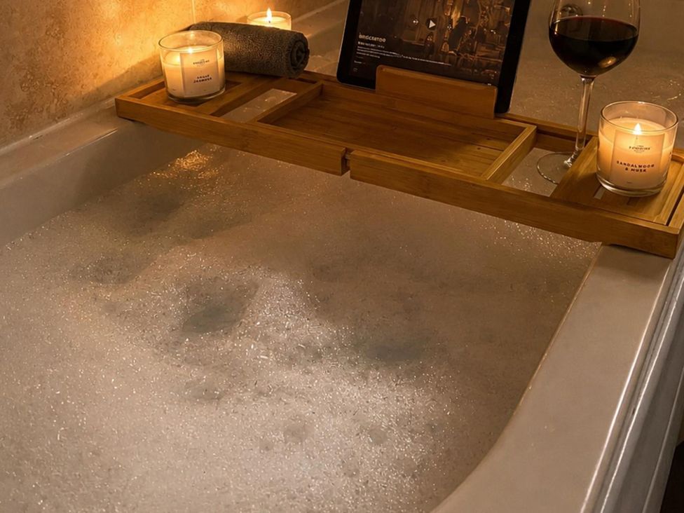 A bathtub with candles, a towel, a tablet, and a wine glass at 3Bed House Sleeps 7 Parking Garden Pets Ok Lytham St. Annes