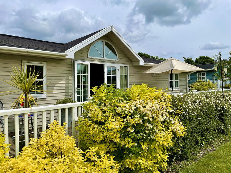 An outdoor view of a house with plants and an umbrella at Stunning Sleeps 6 Luxury Lodge Pets Mercia Marina near Willington, Derbyshire