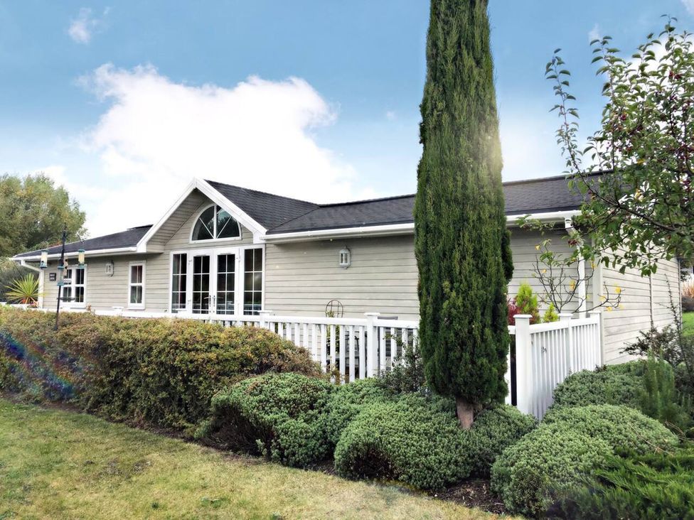 A house with a fence and bushes at Stunning Sleeps 6 Luxury Lodge Pets Mercia Marina near Willington, Derbyshire