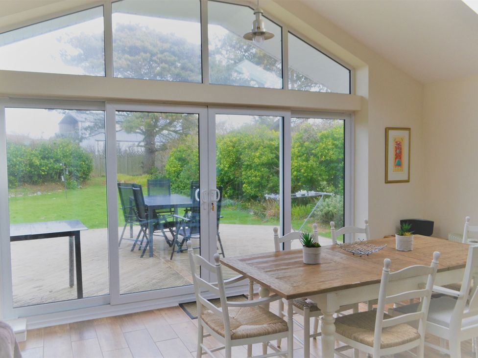 A dining room with a table and chairs overlooking a garden at Sea Side Stay 6 Pet Friendly Parking Garden Rhosneigr