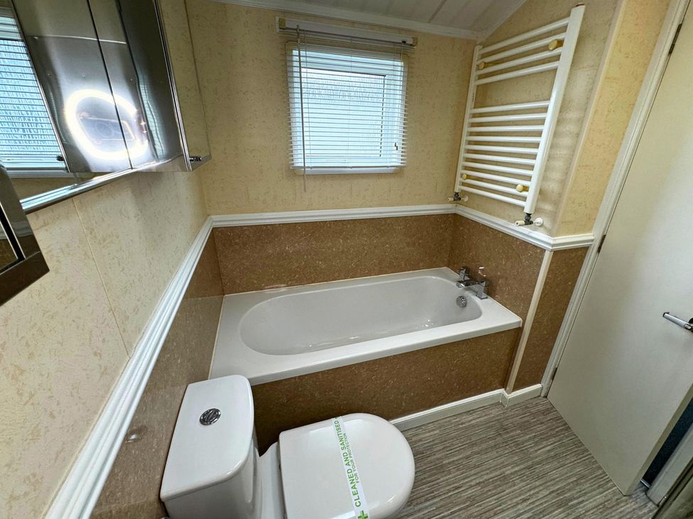 A bathroom with a bathtub, toilet, sink, and mirror at Sunset 5 Southview Holiday Park Skegness