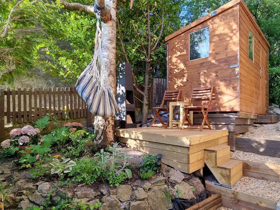 A garden with a wooden shed, chairs, and a hammock