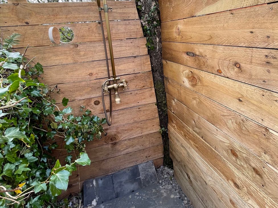 An outdoor shower area with wooden walls and a metal faucet surrounded by ivy at 