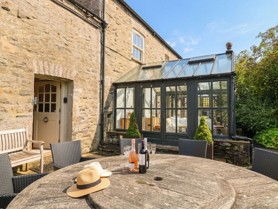 An outdoor area with a wooden table and glass conservatory at Three Mile House in Carnforth