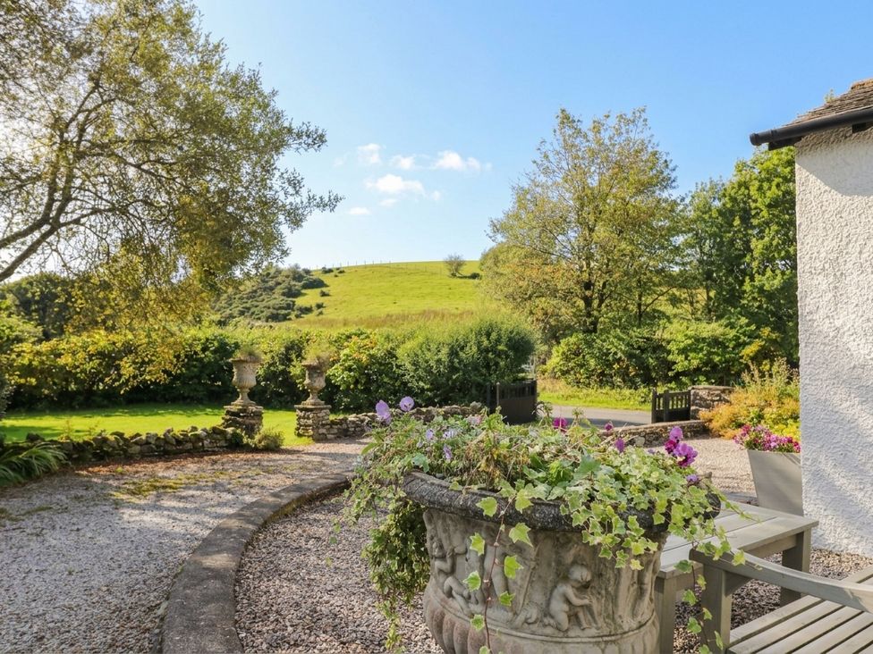 A garden with a stone planter and trees at Three Mile House in Carnforth