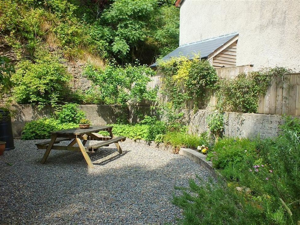 A garden with a gravel area and a wooden table at Llys Gwaun in Fishguard