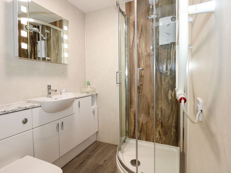 A bathroom with a shower, sink, mirror, and cabinet at Aldena South Snowdon Wharf Porthmadog