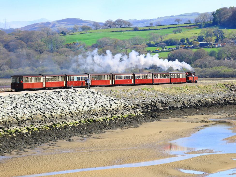 A train with carriages passing by rocks at Aldena South Snowdon Wharf in Porthmadog