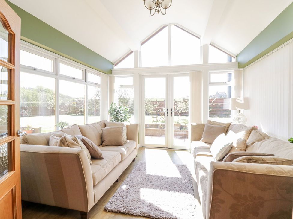 A conservatory with sofas and a rug at Ger Y Mor in Cemaes Bay