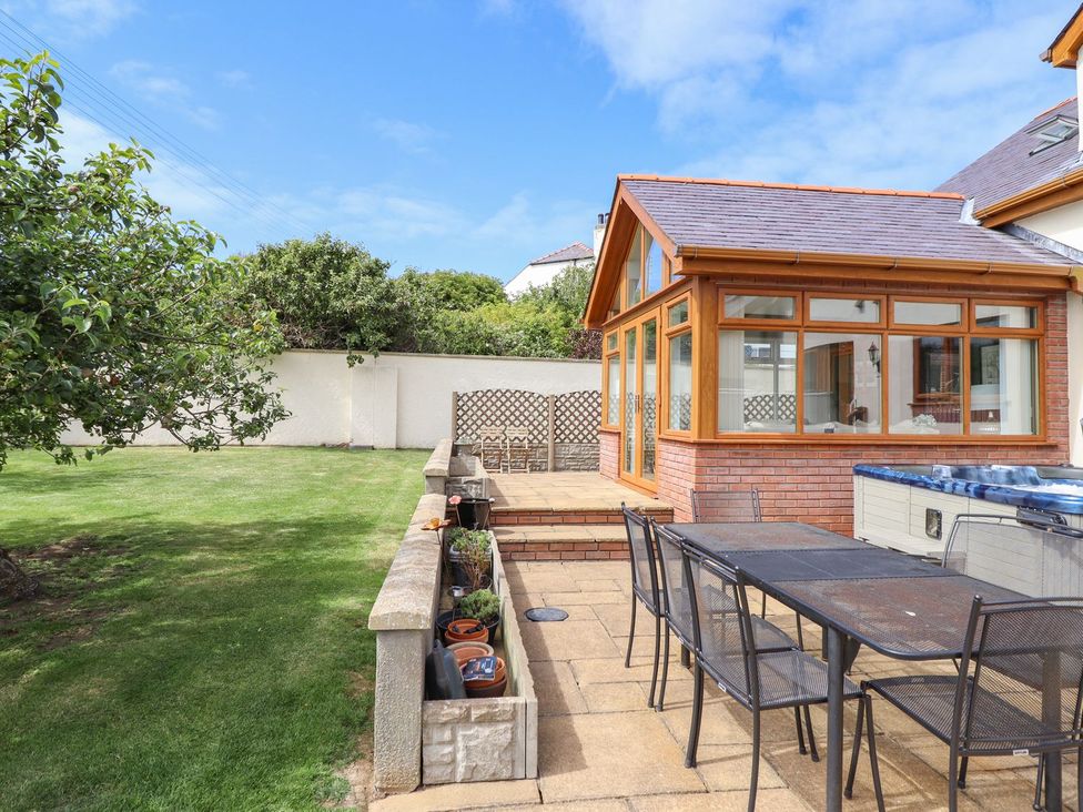 A garden with a conservatory and dining table at Ger Y Mor in Cemaes Bay
