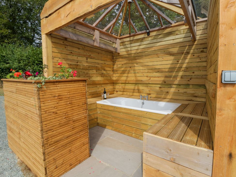 An outdoor bath area with a wooden structure and flowers at Oak Lodge Brecon