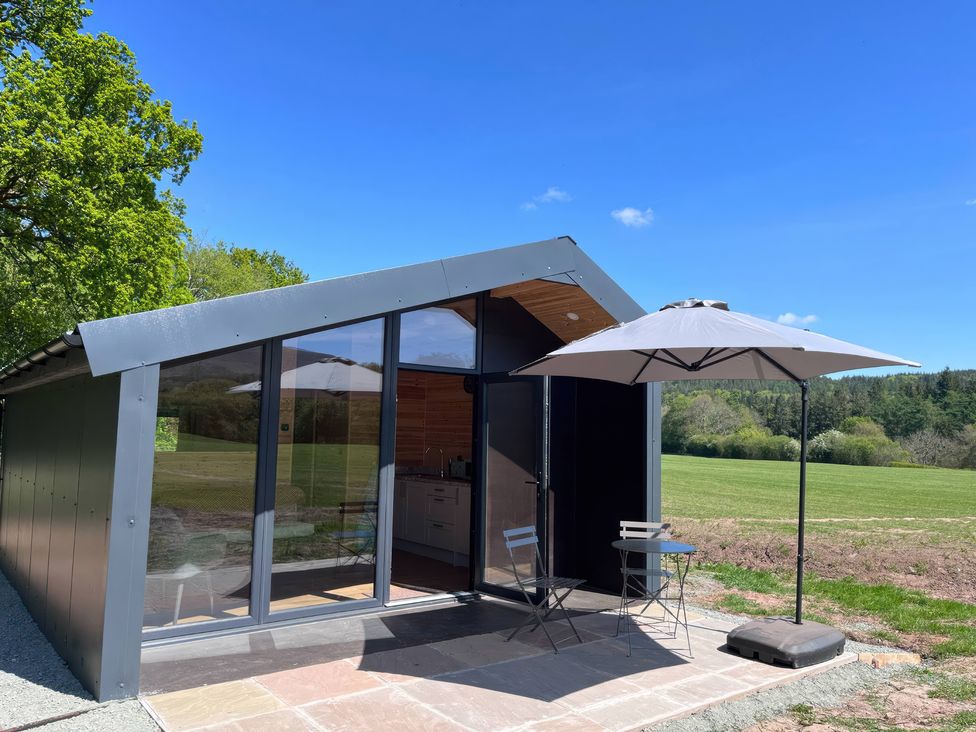 An outdoor seating area with a cabin and an umbrella at Sycamore Lodge in Brecon
