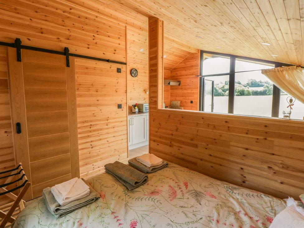 A bedroom with a bed, towels, a kitchenette and a sliding door at Sycamore Lodge in Brecon