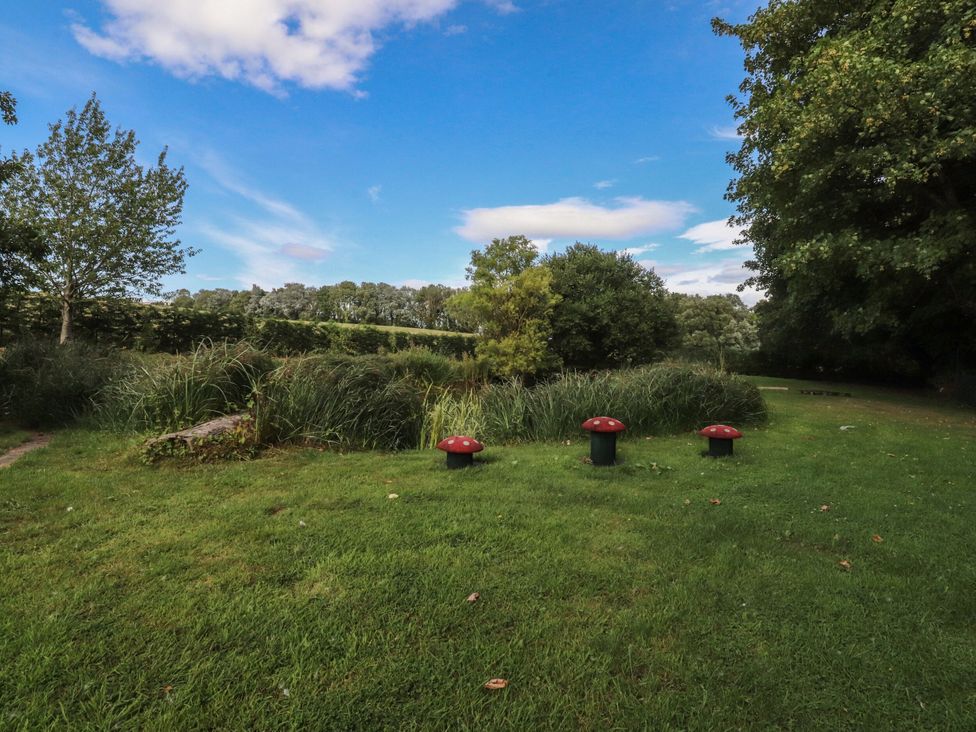 A garden with grass, trees, and mushroom decorations at The Shippon in Burscough
