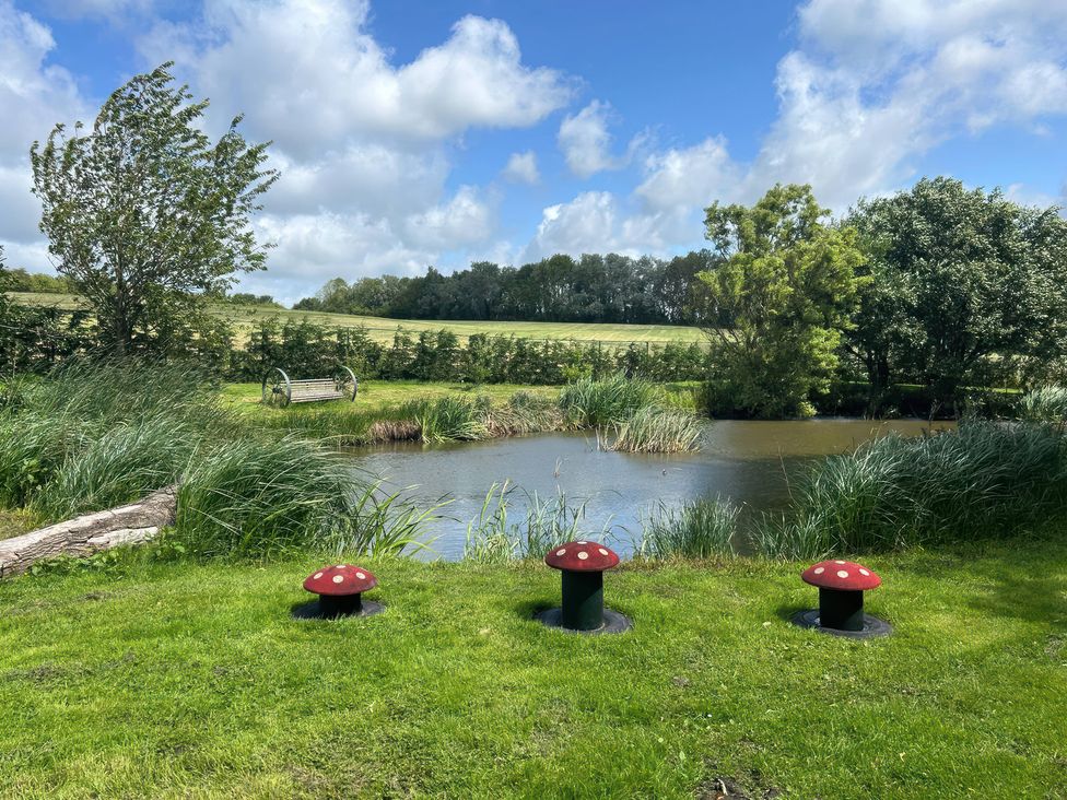 A pond surrounded by grass and trees with mushroom sculptures and a bench at The Log Cabin in Ormskirk