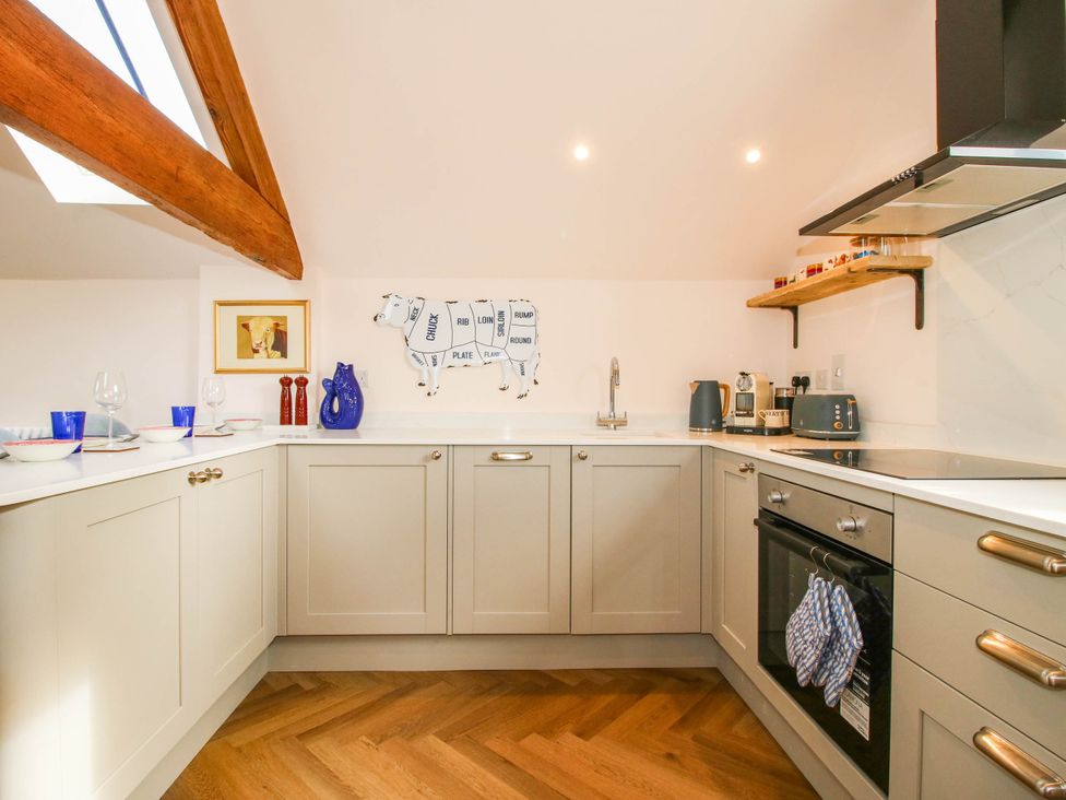 A kitchen with cabinets, sink, oven, and cow decoration at Little Red Barn in Wallop near Westbury