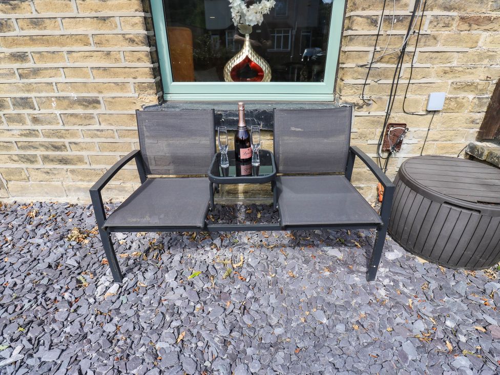 An outdoor seating area with a bench and a wine bottle at Brodie Cottage in Brighouse