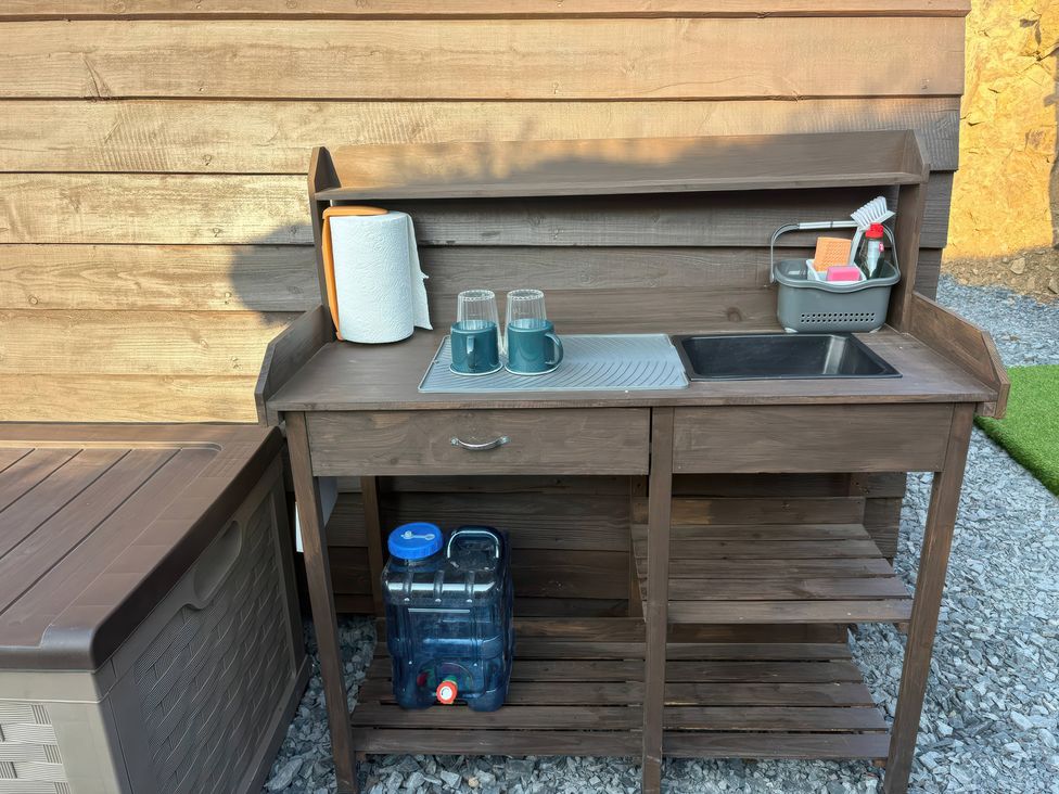 A wooden sink unit with cups and cleaning supplies at Darn Mawr 