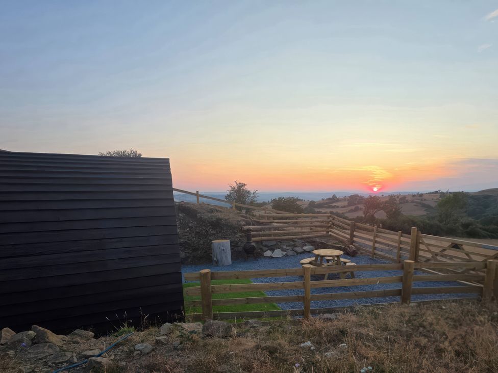An outdoor area with a table and chairs overlooking a sunset at Darn Mawr 