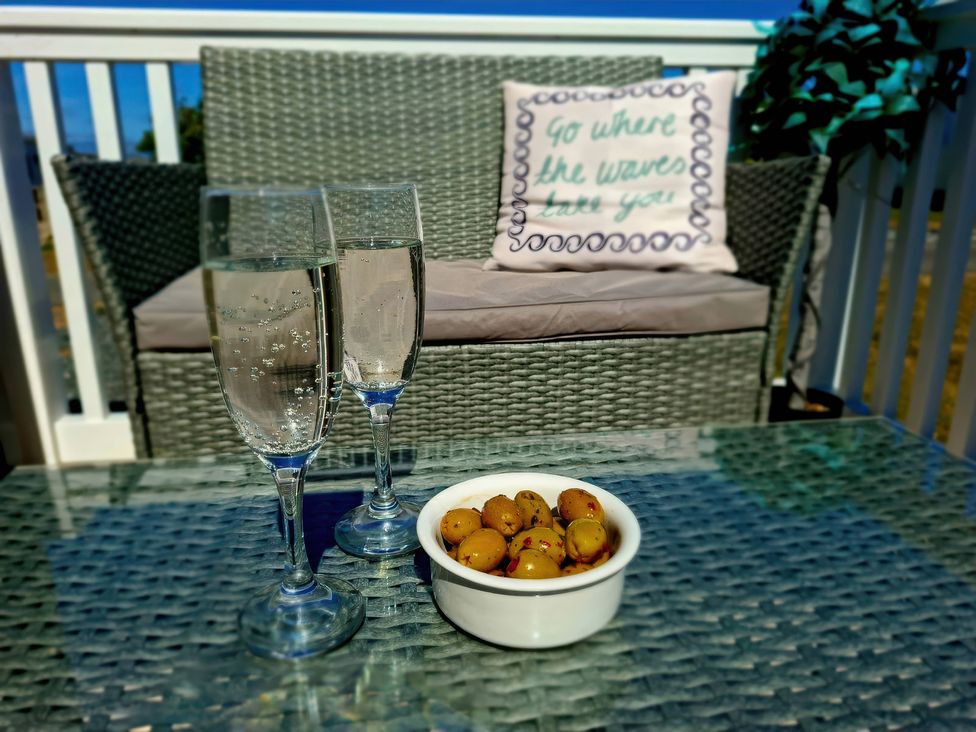 A glass table with two glasses and a bowl of olives at Demelza (B34) Seven Bays Holiday Park in Padstow