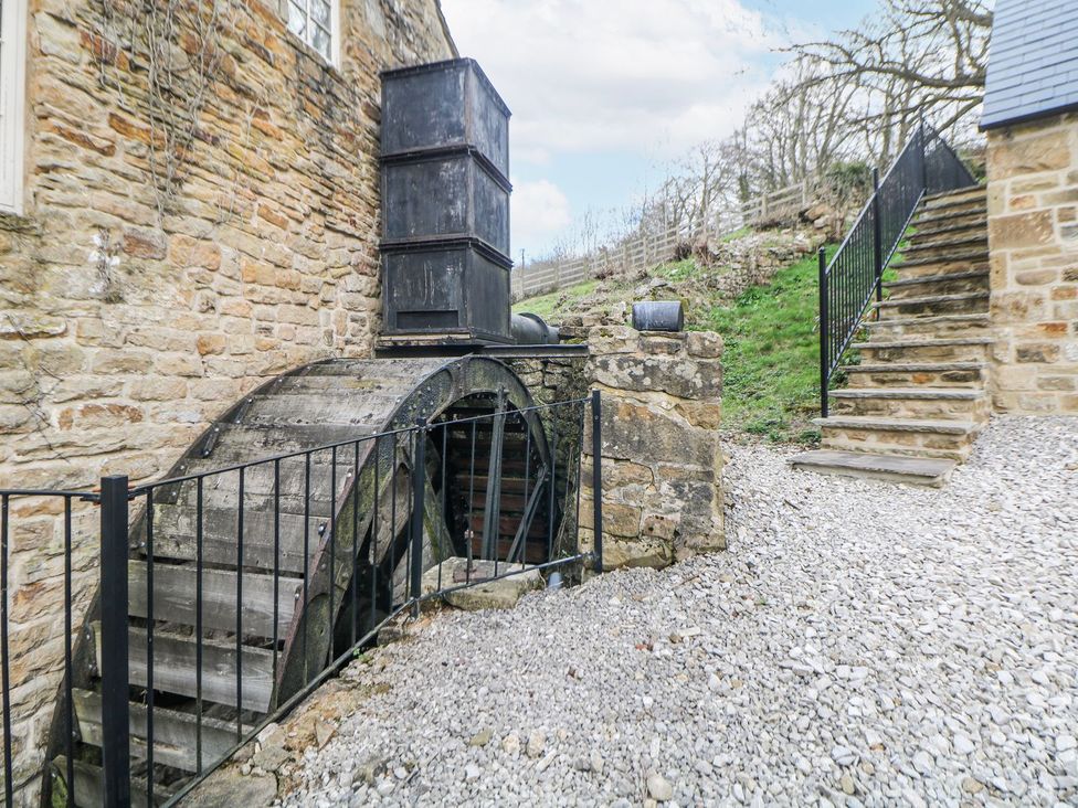 An outdoor water wheel with a staircase and gravel path at Little Mill in Ashover