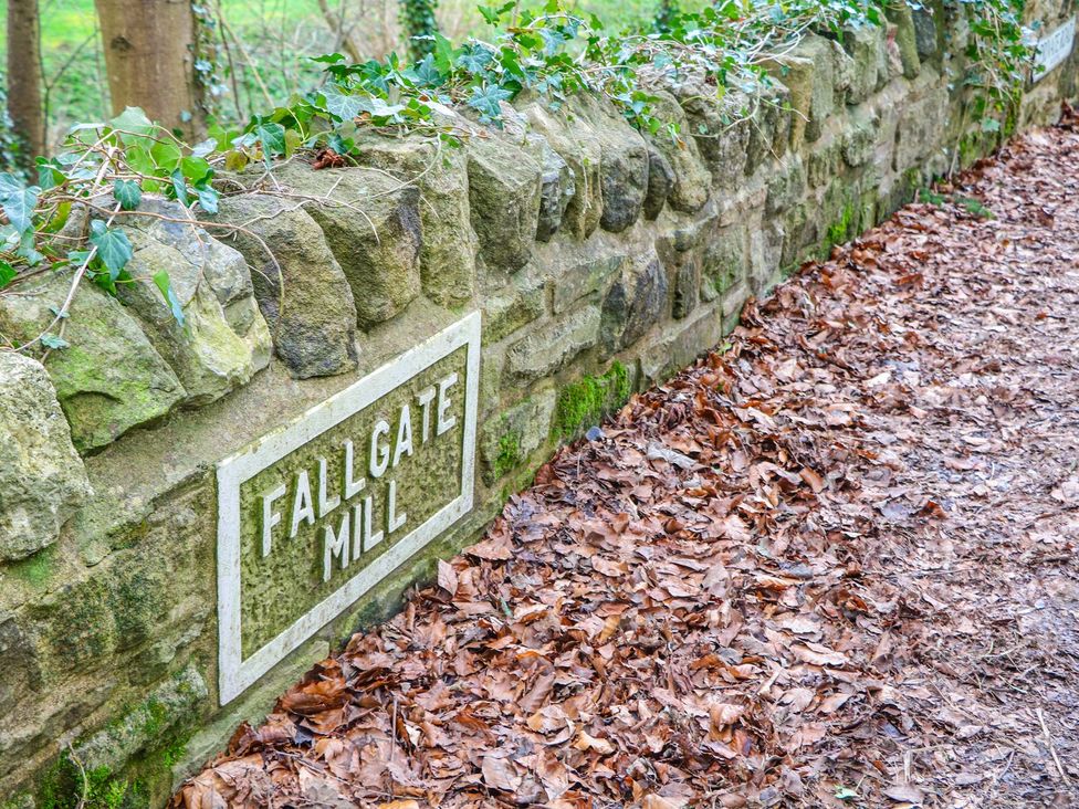 A stone wall with a sign reading Fallgate Mill and leaves on the ground at Little Mill Ashover