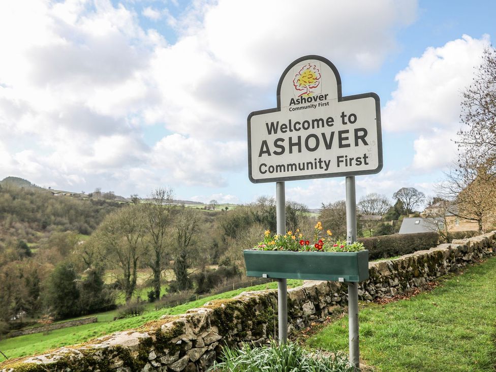 A welcome sign for Ashover with flowers by a stone wall in Ashover