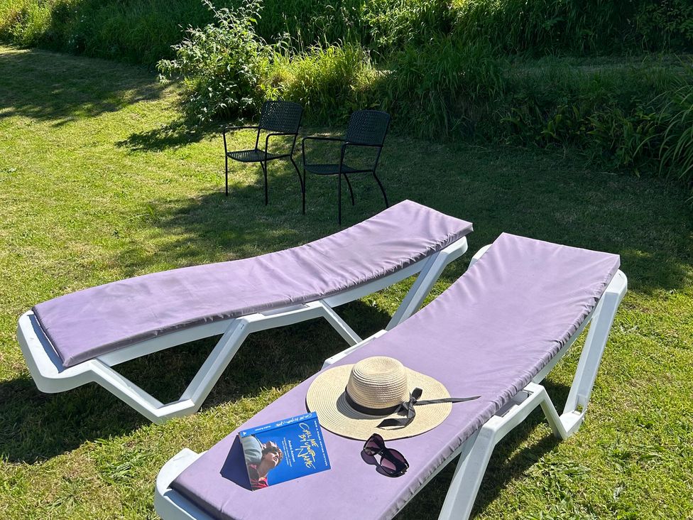 Two lounge chairs with a book, sunglasses, and hat in a garden at The Old Forge in Bickerton near East Prawle